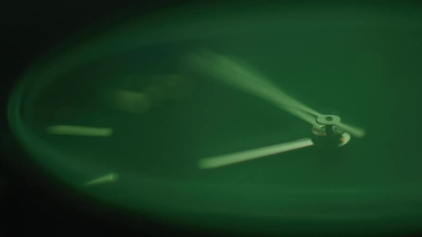 A dark timelapse shows the blurred sweep of the luminous green hands of a watch signifying the rapid passage of time