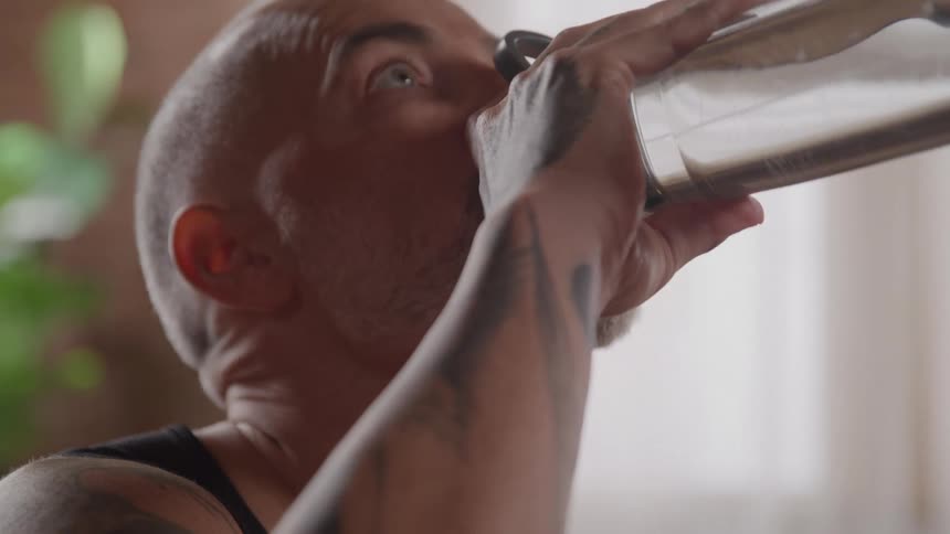 A closeup profile shot shows a tattooed man with a shaved head taking a break from his workout to drink from a water bottle
