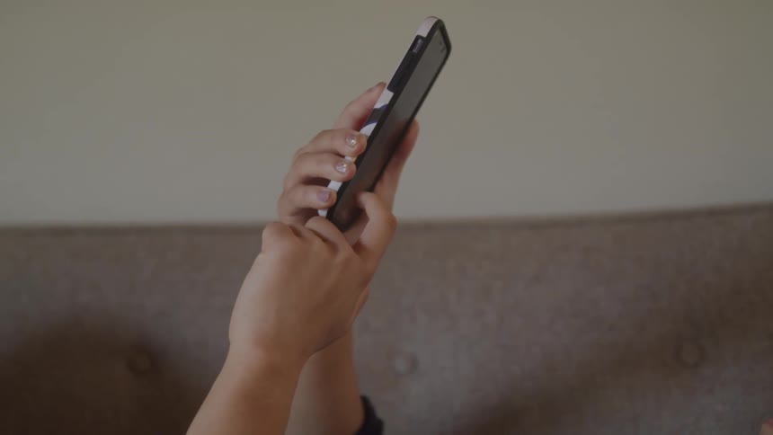 A young woman uses a mobile phone while lying on a couch in a room