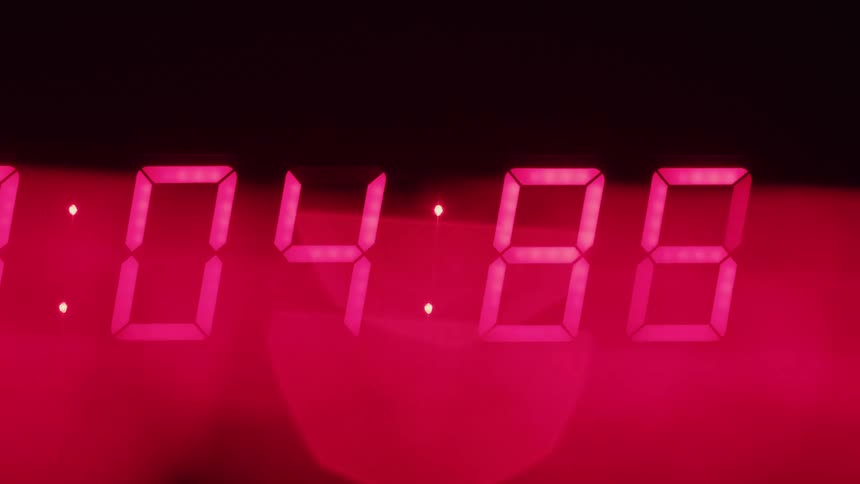 In an extreme closeup the bright red segmented numbers of a digital led timer rapidly count down with the seconds and hundredths of a second ticking away quickly