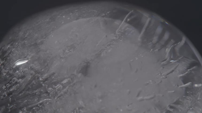 A macro shot reveals the intricate internal cracks and crystallike formations inside a slowly rotating sphere of clear ice