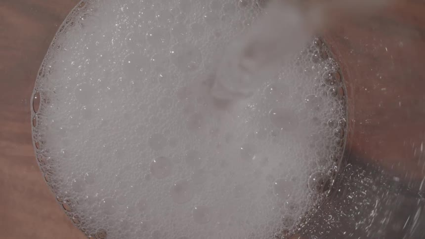 From a topdown view a fizzy carbonated beverage is poured into a glass creating a thick head of white foam and bubbles