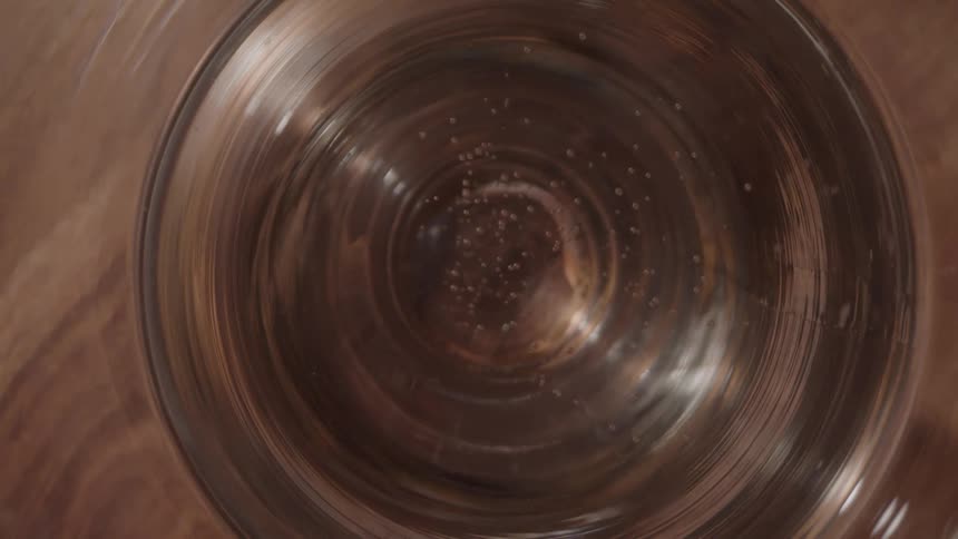 A topdown view shows small bubbles rising to the surface of a carbonated beverage in a glass resting on a wooden table