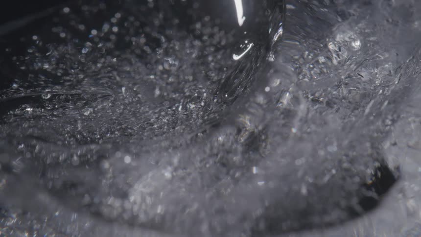 A macro shot captures the detailed textures and trapped air bubbles within a slowly rotating piece of ice against a dark background