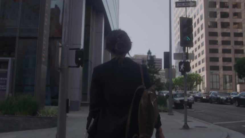 Woman with a backpack walking on a sidewalk in a commercial urban area