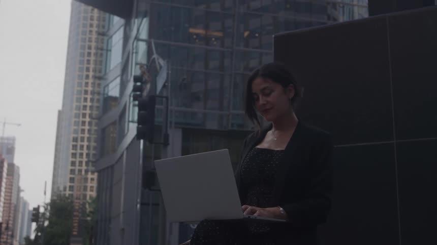 The woman types on her laptop outside the buildings