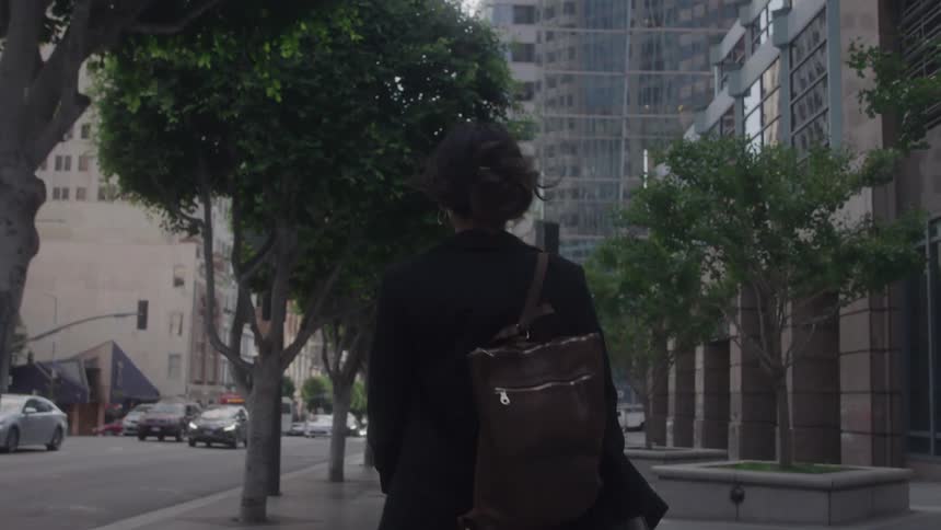 The woman walks on the sidewalk past the buildings