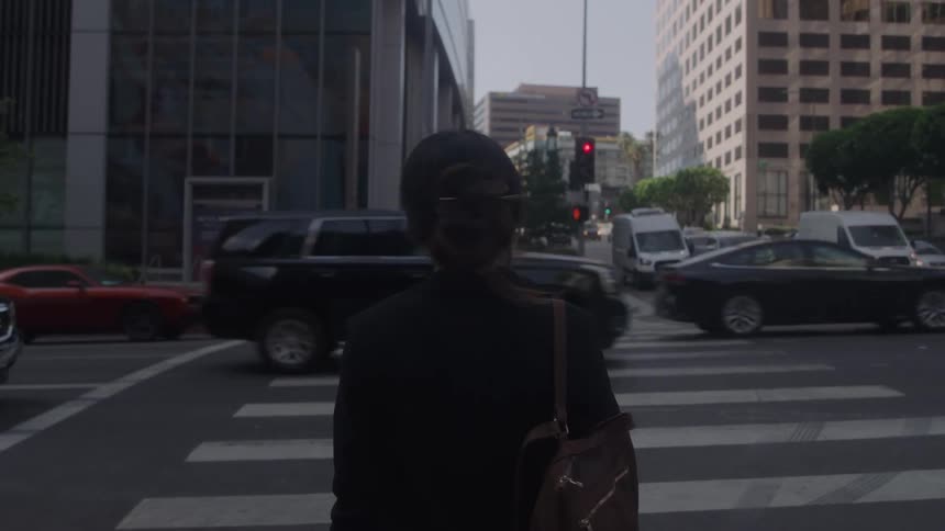 A woman stands at a crosswalk in a city