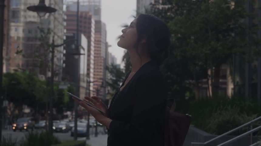 Woman holding a tablet looks up on a busy urban street