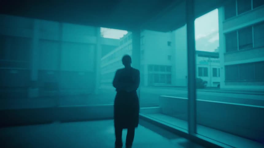 A woman in a power stance standing in the corner of the ground floor of a building with glass walls