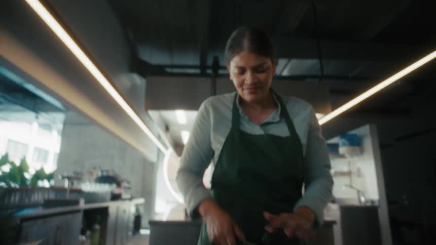 A woman in an apron in a large industrial kitchen preparing food
