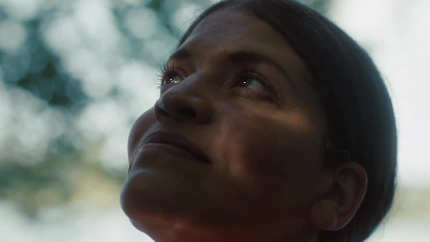 The woman smiles while looking up at the tree