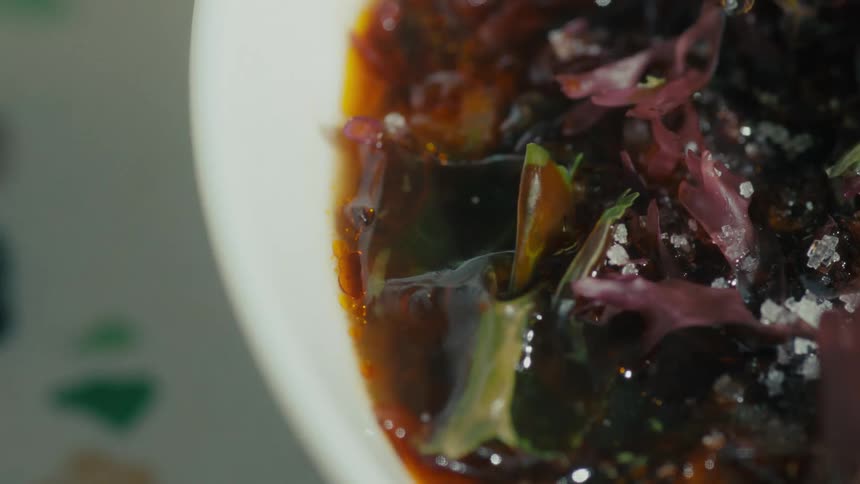 Sprinkling of coarse salt over dark broth garnished with seaweed