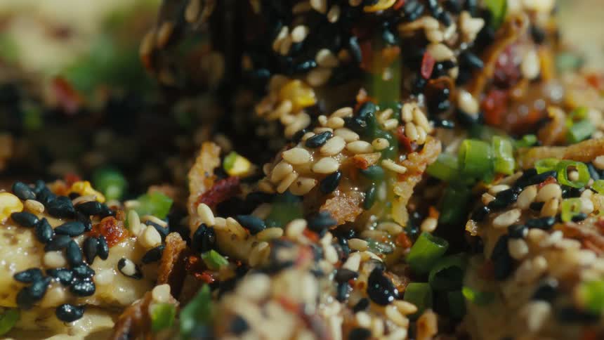 Closeup of food being sprinkled with chopped green herbs
