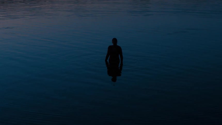 Silhouetted person stands in calm water during dusk
