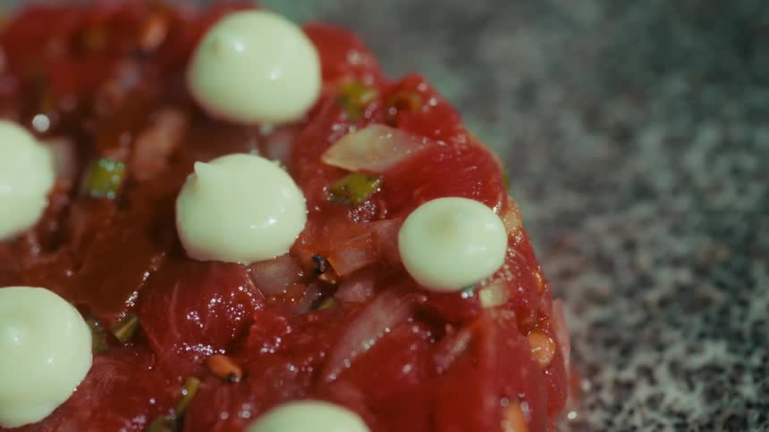 Closeup of a vegan tartare dish topped with aioli on a granite surface