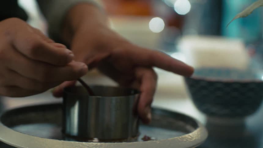 A chef carefully plates food using a metal ring mold