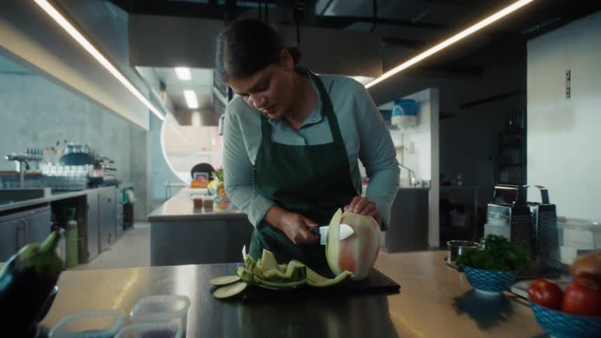 A chef slices a melon on a cutting board in a professional kitchen