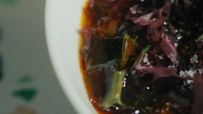A closeup of a rustic healthy dish of leafy greens and dark rich sauce with steam rising from the bowl
