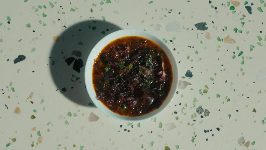 A hand serves a bowl of a rich dark soup