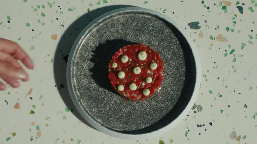 A hand serves a plated gourmet vegan dish with garnishes on a textured plate