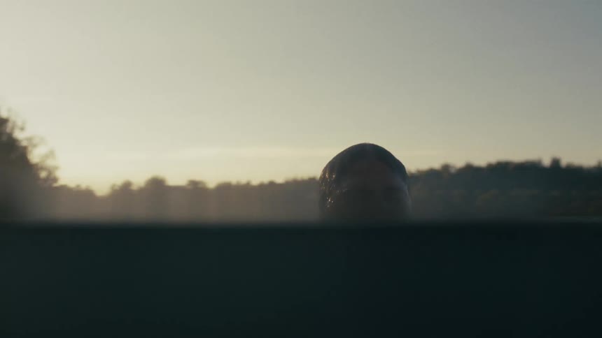 A womans head rising from below the water in a body of water near a forest