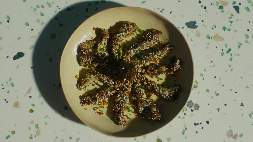 A hand serves a plate of seasoned strips of eggplant