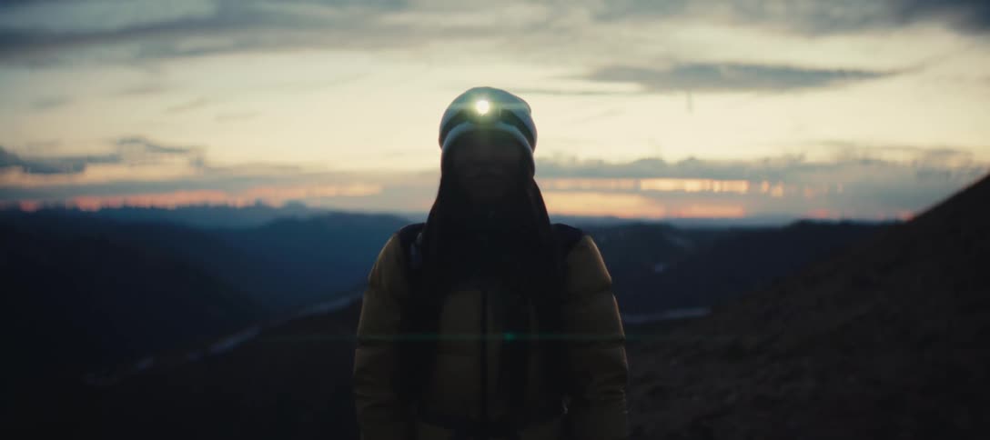 A person standing on the side of a mountain wearing a cap and a lantern on their head