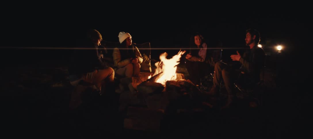 Group of friends gathered around a campfire at night