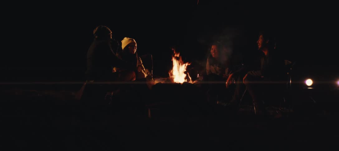A group of friends sitting around a campfire talking and laughing