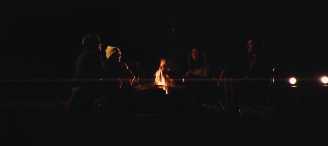 The fire rises as friends talk around it