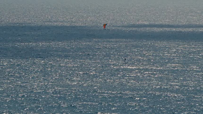 A person standing on a surfboard in the ocean using a small parachute to catch the wind and ride the board