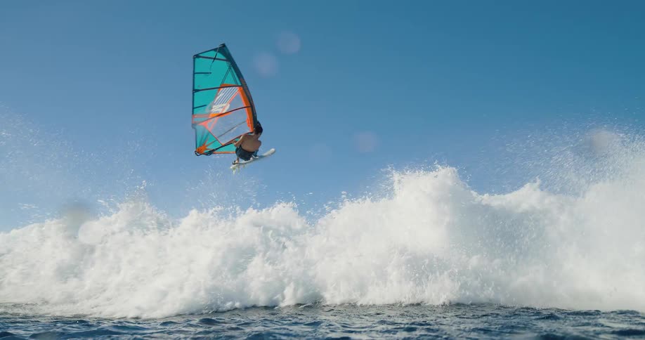 People windsurfing on waves with colorful sails standing out against the blue sky