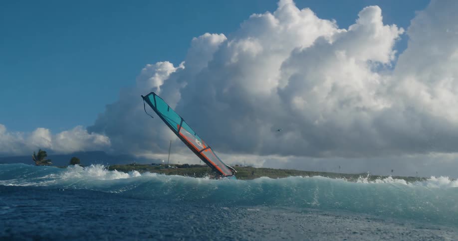 A man is wind surfing along a coast with medium waves