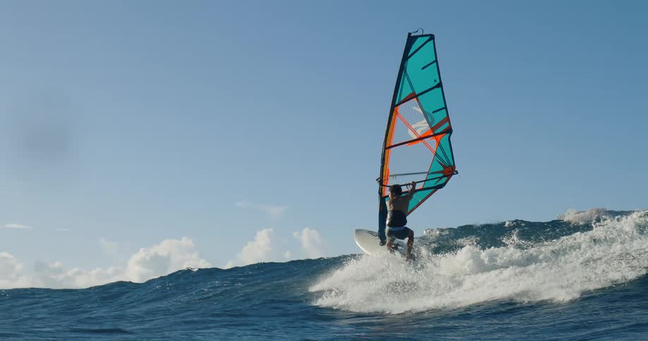 Windsurfer rides a wave with a colorful sail in the open sea