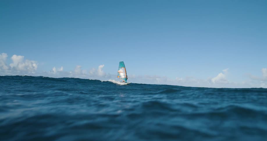 Person windsurfing alone in the open sea standing out against the blue horizon