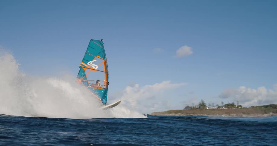 A windsurfer rides a large ocean wave under a clear blue sky