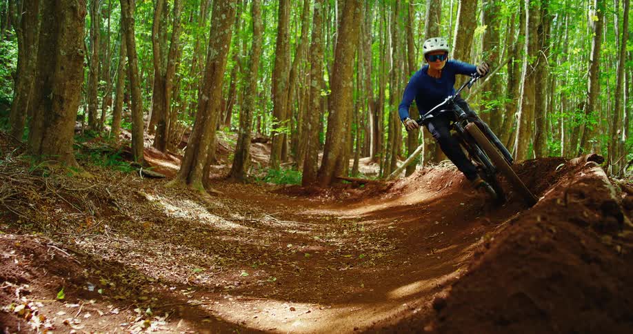A rider carves a berm on winding singletrack through tall woods