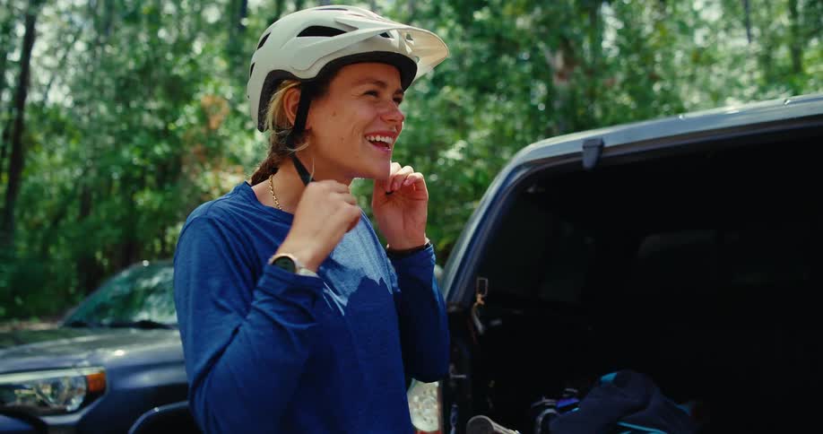 The woman smiles while removing her bike helmet
