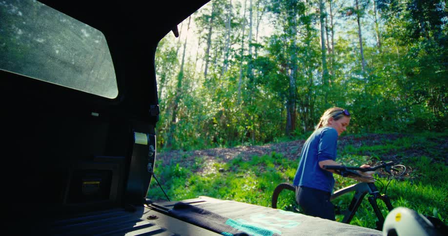 The woman removes a bicycle from the back of the vehicle
