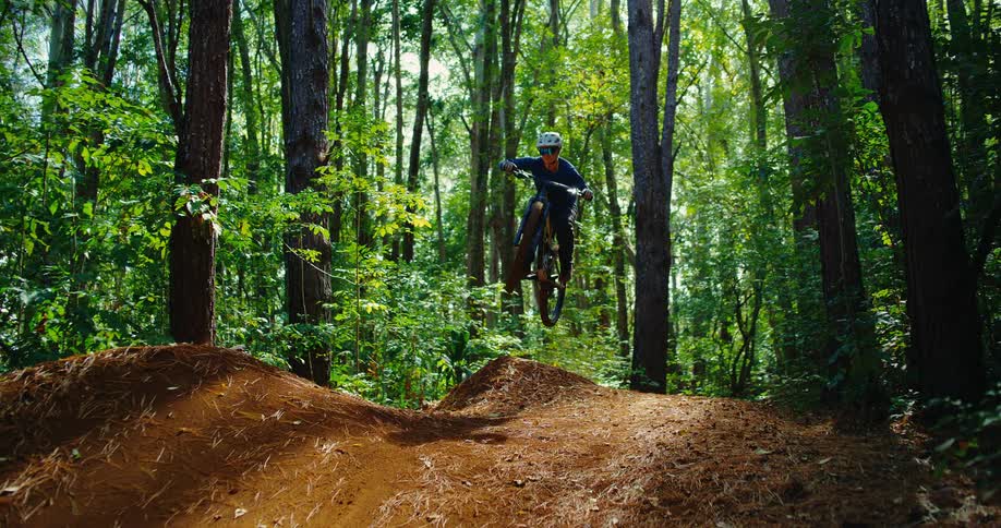 A man on a bicycle doing a jump over a bump on a trail in a forest