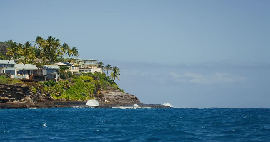 Large houses surrounded by trees on a promontory with the ocean gently crashing on the rocks below