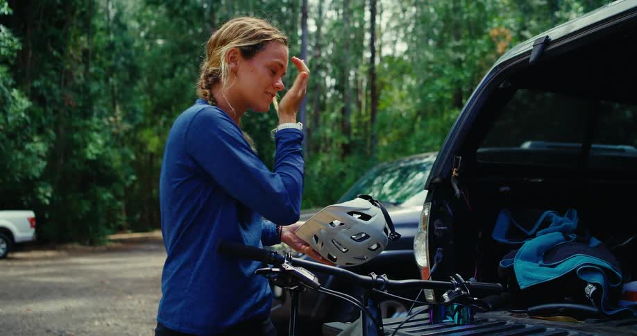 Woman takes off her helmet and puts it in the trunk of her car after cycling and puts on a cap