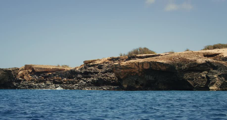 A rocky coastal cliff meets the blue ocean under a clear sky