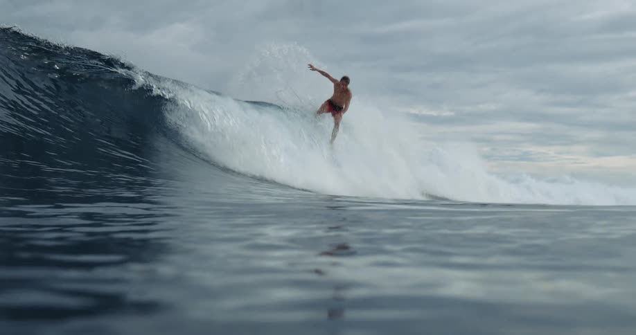 A wide shot captures a person surfing a large wave the shot is from the water showing the surfer riding the wave toward the camera