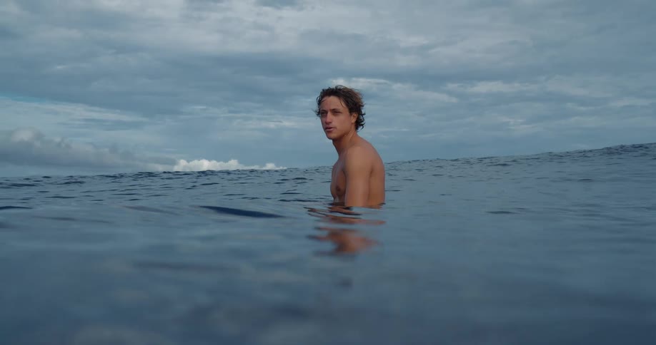 Man in the sea with surfboard looking with calm expression