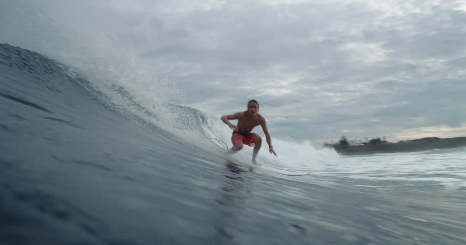 A person surfs along a large wave on a surfboard as the camera follows them the surfer rides the wave and then disappears behind it
