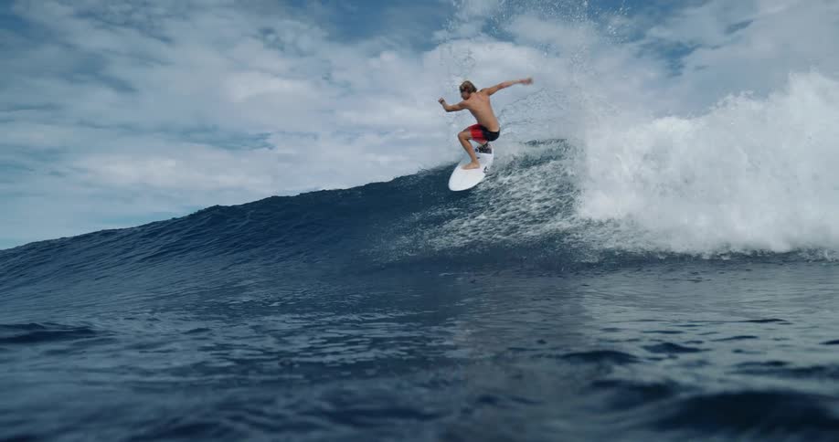 A surfer rides a wave while others paddle nearby in the ocean