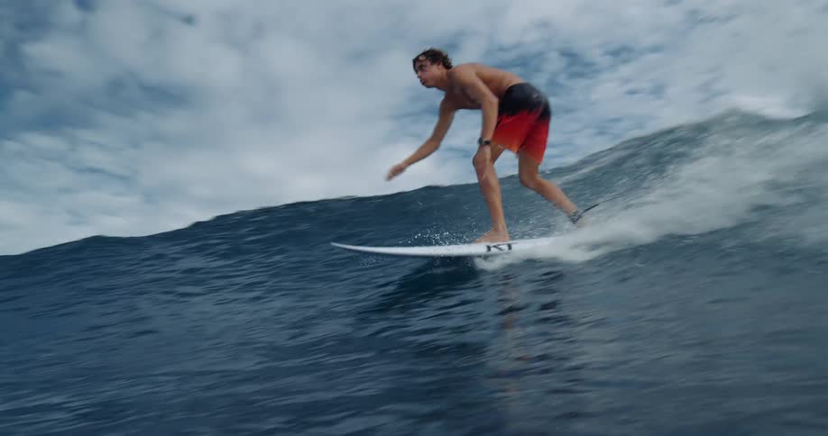 A surfer carves along a large wave on a cloudy day creating a foamy wake behind his board the camera is at the same level as the water capturing the action from a low dynamic angle