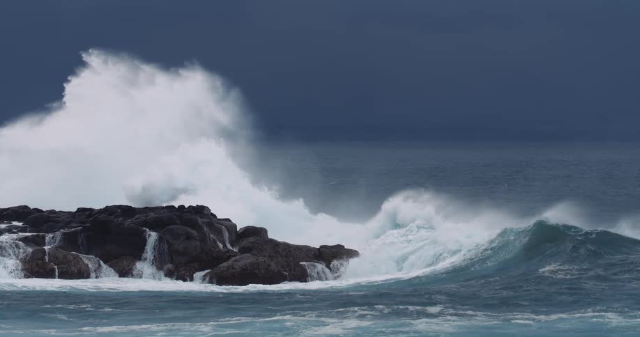 Crashing ocean waves hit dark coastal rocks under a stormy sky
